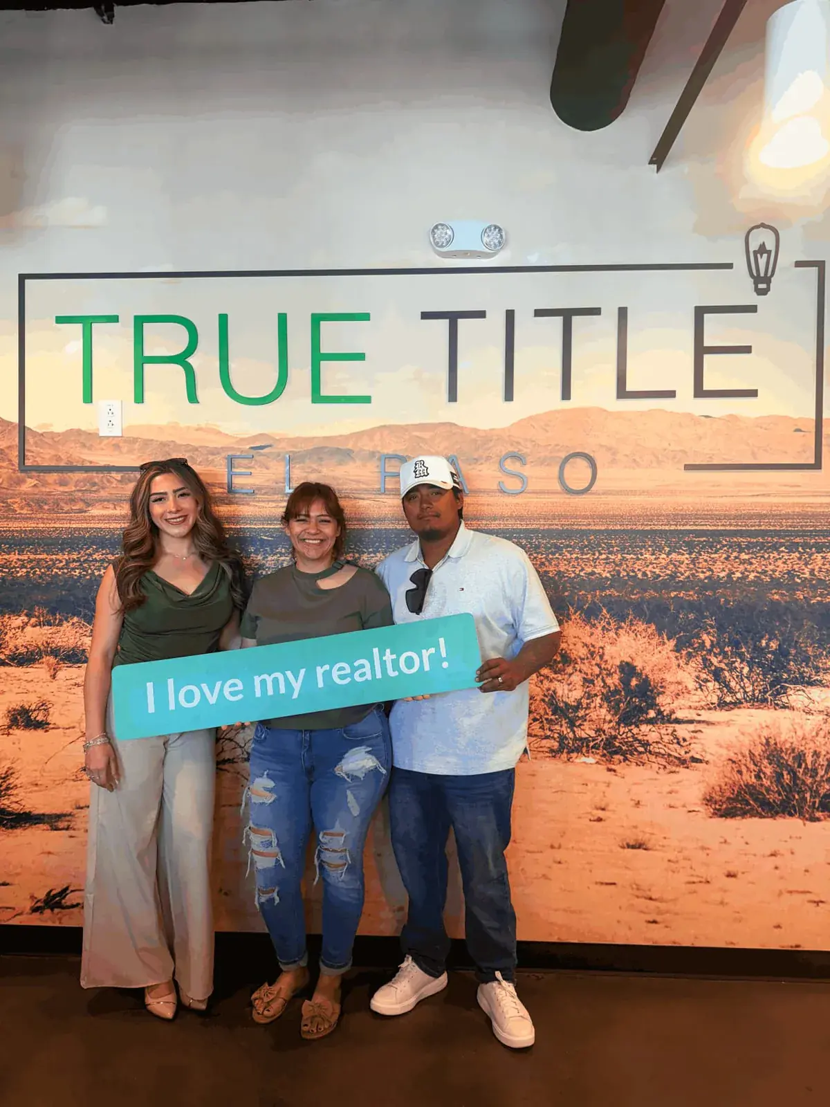 Ximena Martinez with two clients holding an “I love my realtor!” sign
